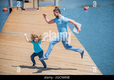 Springen Sie frei. Energischer Vater und Sohn springen auf den Pier. Spaß für die ganze Familie Stockfoto