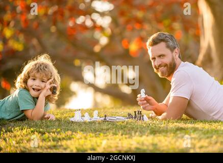 Glückliche Familie von Vater und Sohn Kind spielen Schach auf grünem Gras im Park im Freien, Schachmann Stockfoto