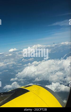 Vertikale Aufnahme eines blauen Himmels mit schwebenden weißen Wolken aus einem Flugzeugfenster Stockfoto