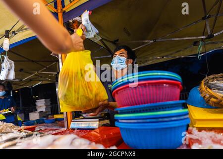 Street Food Nachtmarkt in Putrajaya, in der Nähe von Kuala Lumpur. Verkäufer mit Gesichtsmaske in einem Seafood Street Store übergibt die Plastiktüte mit frischem Meer Stockfoto