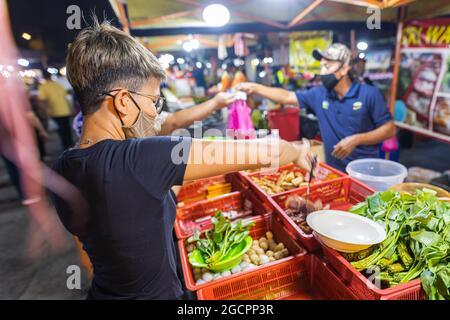 Street Food Nachtmarkt Putrajaya, in der Nähe von Kuala Lumpur. Junge asiatische Mädchen kauft Gemüse in einem Nachtmarkt. Malaysische Frauen mit Gesichtsmaske in einer Straße Stockfoto