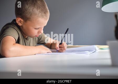 Der Junge sitzt am Tisch und macht zu Hause Schularbeiten. Homeschooling Konzept. Stockfoto