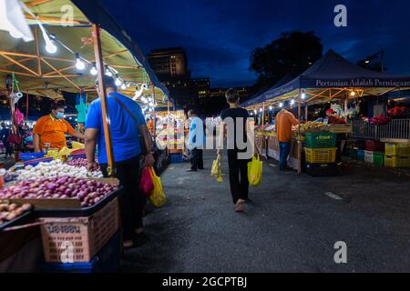 Street Food Nachtmarkt in Putrajaya, in der Nähe von Kuala Lumpur. Die junge Frau geht zwischen den Essensständen und trägt ihre Einkäufe in gelben Plastiktüten Stockfoto