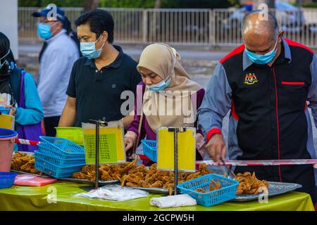 Muslimische malaysische Frau in einem frittierten Hühnerladen auf dem Straßenmarkt sucht nach den besten Stücken Malaiische Dame mit Hijab und Gesichtsmaske Kauf Huhn wi Stockfoto