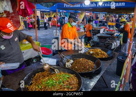 Gebratene Nudeln werden auf einem Nachtmarkt in Kuala Lumpur gelagert. Zwei na verkaufen traditionelle Nudeln aus einem Wok. Aufgrund der Corona-Krise trägt der Mann Gesicht ma Stockfoto