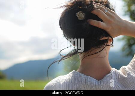 Ein Mädchen hält ihr Haar mit der kleinen Blume in der Hand. Natürliche Frisur Stockfoto