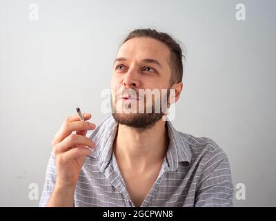 Kaukasischer Mann in grauem Hemd raucht eine Zigarette im Weißen Zimmer in Medellin, Kolumbien Stockfoto