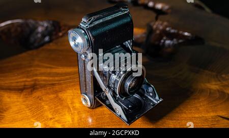 Leipzig, Sachsen, Deutschland - 1. Oktober 2020: Alte zerkratzte und staubige Fotokamera, mit zusammenklappbarem original Carl Zeiss Objektiv, auf einem antiken Holztisch. Stockfoto