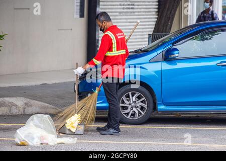 Kuala Lumpur, Malaysia - 04. Oktober 2020: Straßenkehrmaschinen auf den Straßen von Kuala Lumpur. Ein alter asiatischer Mann putzte die Straße und den Seitenweg mit einem Reis Stockfoto