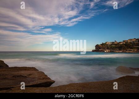 Die felsige Küste rund um Bondi Beach, Sydney, Australien. Wellen, die auf die Felsen im Wasser plätschern. Tamarama Point mit Blick auf Tamarama Beach. Whit Stockfoto