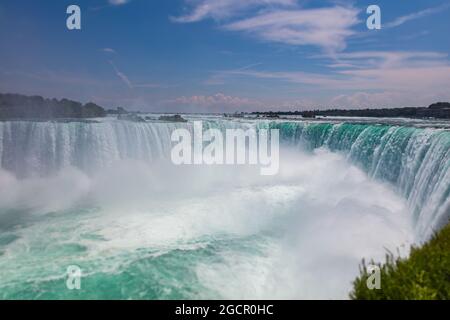 Blick auf die beeindruckenden Niagarafälle. Hufeisen fällt von der kanadischen Seite der Fälle. Massives Wasser fällt unter den wolkigen Himmel. Spritzer Stockfoto