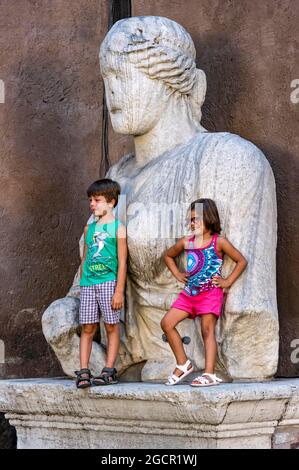 Kinder posieren an der alten römischen Kolossalstatue Madama Lucrezia, Piazza San Marco, Rom, Latium, Italien Stockfoto