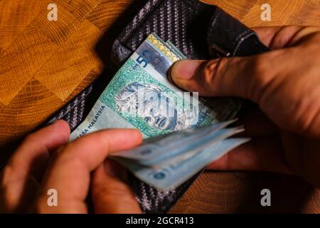 Männliche Hände zählen 50 Ringgit Malaysia in einer Ledertasche auf einem Holztisch. RM50 in Mans Hand. Malaysischer Ringgit, der von einem jungen Mann in einer Brieftasche gezeigt wird. Cl Stockfoto