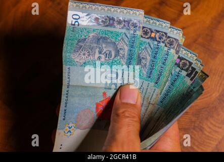 Eine Sammlung von fünfzig malaysischen Ringgit-Banknoten in einer männlichen Hand. Man Hand zeigen Malaysia Ringgit Banknoten. Jungen Hände halten Geld von Malaysia. Asien Stockfoto