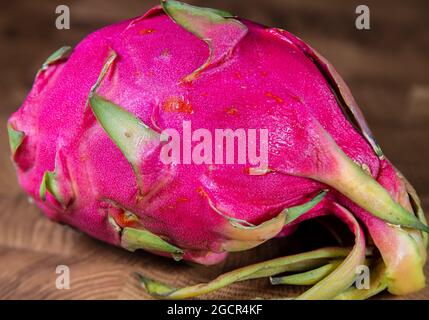 Nahaufnahme einer roten rosa Drachenfrucht auf Holzhintergrund Makrofotografie einer reifen Pitaya. Drachenfrucht auf einem Holztisch. Stockfoto