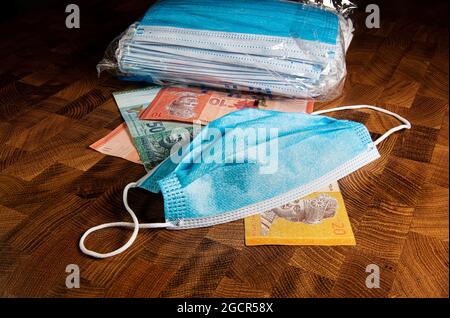 Gesichtsmasken, die neue Weltwährung im Jahr 2020. Corona Cov19 Crisis macht Gesichtsmaske für die am meisten gesuchte Ausrüstung. Steigende Preise. Mundmaske mit Geld auf Stockfoto