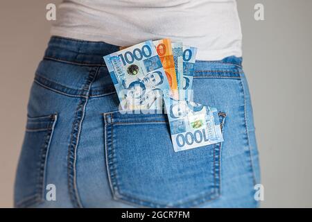 Philippines Peso in einer weiblichen Jeanshose. Philippinische Pesos-Notizen stecken in einer Jeans-Tasche. Pesos in der Gesäßtasche einer Denim-Hose für Mädchen. Geld i Stockfoto