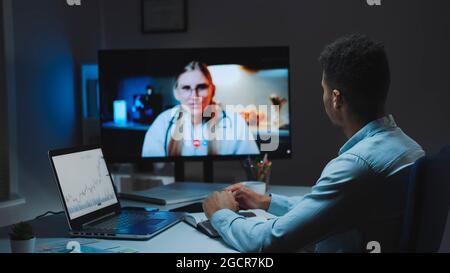 Rückansicht des jungen Mannes, der Videoanruf mit der Ärztin über Ihre Gesundheit in der Nacht macht und Analyse am Computer macht Stockfoto