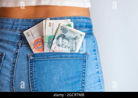 100 Chines Yuan in einer weiblichen Jeanstasche. China-Banknoten stecken in einer Jeans-Tasche. Renminbi in der Gesäßtasche einer Denim-Hose für Mädchen oder Frauen. Stockfoto