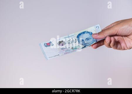 Singapur-Dollar in weiblicher Hand. Die Hände der Frau zeigen singapurische Dollar-Banknoten. Mädchen halten Geld von Singapur. Asiatische Währung. Nahaufnahme Stockfoto