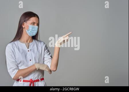 Ärztin in weißem Mantel und medizinischer Maske zeigt Kopierraum Stockfoto