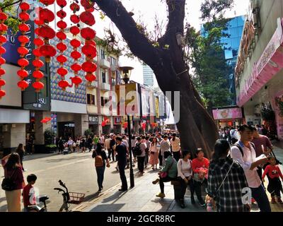 Alte Damen sitzen unter einem riesigen Baum an der Beijing Road in Guangzhou mit vielen Touristen vor dem vietnamesischen Restaurant Tiger Prawn. Stockfoto