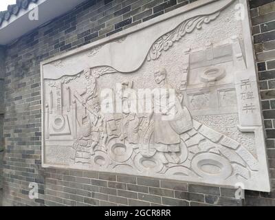 Kunst in den Straßen von Guangzhou in der Nähe von historischen Stätten mit einem hängenden Denkmal an einer Ziegelmauer, das eine Familie zeigt Stockfoto