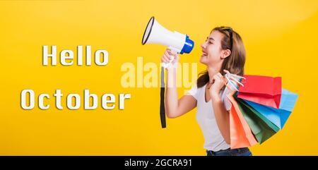 Hallo Oktober, Portrait Asian schön glücklich junge Frau lächelnd halten Einkaufstaschen bunt und schreiend in Megaphon sie auf Seite weg, st Stockfoto