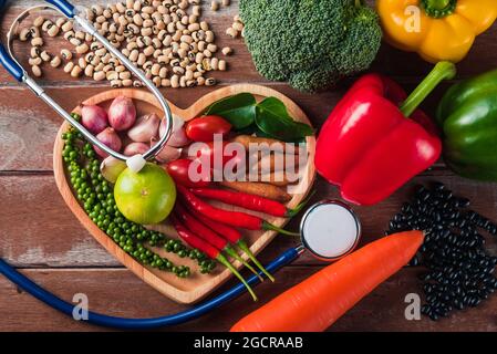 Weltessen-Tag, Draufsicht auf verschiedene frische Bio-Obst und Gemüse in Herzplatte und Arzt Stethoskop mit Kopierer Platz, Studio auf Holzregale aufgenommen Stockfoto