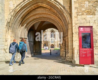 Ein paar Besucher gehen durch den gewölbten Eingang zu den Bezirken und der Kathedrale von St. Peter, St. Paul und St. Andrew in Peterborough, England. Stockfoto