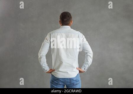 Rückansicht des Mannes im Denim-Hemd, der Hände auf Hüften auf grauem Hintergrund isoliert hält Stockfoto