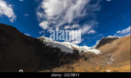 Berggipfel in Tibet - Kangbu-Gletscher auf 5200 Meter über dem Meeresspiegel. Weiße Wolken und blauer Himmel über den hohen Bergen des Himalaya. Schnee auf dem Gipfel Stockfoto