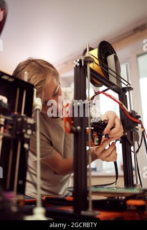 Von oben junger Mann, der während der Arbeit in der Werkstatt einen Teil des modernen 3D-Druckers justiert Stockfoto