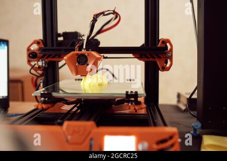 Gelbes Modell aus gelbem Kunststoff und auf einem modernen 3D-Drucker auf einem Tisch in der Werkstatt platziert Stockfoto