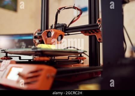 Gelbes Modell aus gelbem Kunststoff und auf einem modernen 3D-Drucker auf einem Tisch in der Werkstatt platziert Stockfoto