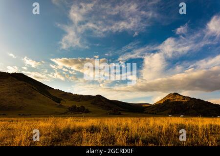Die Sonne geht in der Mongolei unter, Landschaftsfotografie bei Sonnenuntergang in der mongolischen Steppe bei Arhangai-Aimag. Blauer Himmel mit weißen Wolken und gelber Steppe g Stockfoto