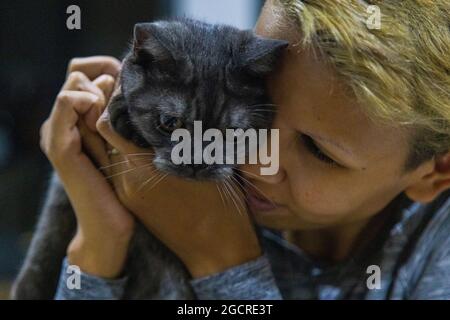 Tierische und menschliche Liebe. Schwarze Kätzchen werden von seinem Besitzer kuschelt. Die blonde Frau drückt zärtlich ihren Kopf gegen die junge Katze Stockfoto