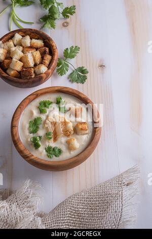 Frisch zubereitete weiße Blumenkohlcremesuppe mit frischen grünen Kräutern und Croutons in Holzschüsseln auf Holztisch. Leinenserviette und Koriander an der Seite. Vert Stockfoto