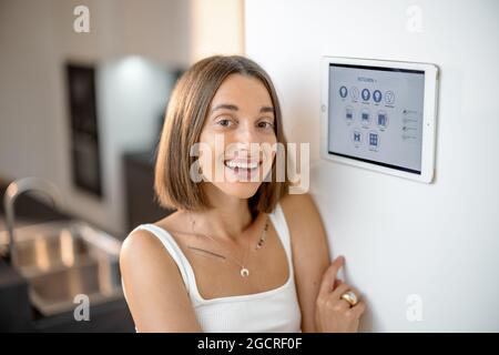 Glückliche Frau, die intelligente Geräte über das Bedienfeld in der Küche steuert Stockfoto