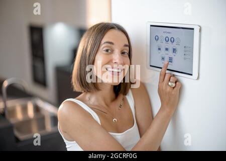 Glückliche Frau, die intelligente Geräte über das Bedienfeld in der Küche steuert Stockfoto