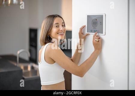 Glückliche Frau, die intelligente Geräte über das Bedienfeld in der Küche steuert Stockfoto