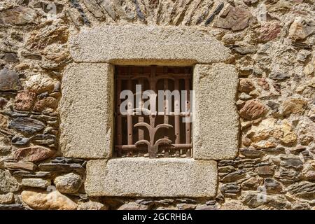 Kleines Fenster in einer Steinmauer, geschützt durch eine mit Filigran verzierte Schmiede Stockfoto