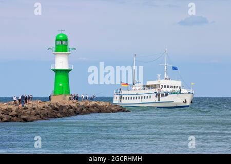 Ausflugsboot am grünen Leuchtturm an der Spitze des Wellenbrechers des Hafens von Warnemünde vorbei. Stockfoto