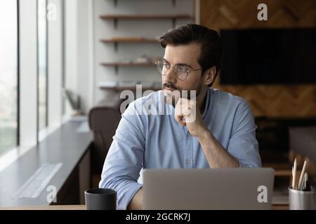 Nachdenklicher Geschäftsmann mit Brille, der vom Arbeitsplatz aus auf das Fenster blickt Stockfoto