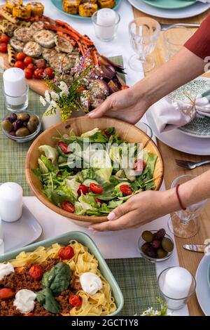 Hände einer jungen Frau, die eine Schüssel mit vegetarischem Salat auf den Tisch legte, serviert zum Familienessen Stockfoto