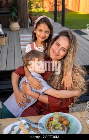 Fröhliche Kinder und ihre hübsche Mutter essen beim Landhaus Stockfoto