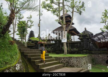 Frau im gelben Sarong, die die Treppe des heiligen Besakih-Tempels begeht. Bali, Indonesien. Stockfoto