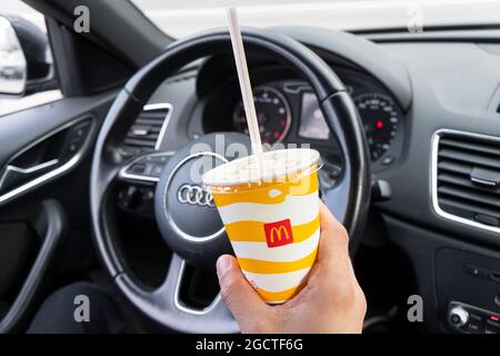 Sankt-Petersburg, Russland, 9. August 2021: Fahrerhand hält McDonalds Papierbecher mit einem Stroh. Hand mit einem Coca-Cola-Getränk im Audi Q3. Stockfoto