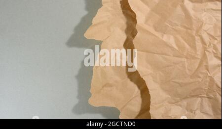 Mintbraunes Stück Papier mit abgerissenen Kanten und Schatten auf grauem Hintergrund. Abstrakter kreativer Hintergrund für Designer, Kopierbereich Stockfoto