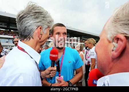 Lukas Podolski (GER) Fußballspieler am Start mit Damon Hill (GBR) Sky Sports Presenter (links) und Johnny Herbert (GBR) Sky Sports Presenter (rechts). Großer Preis von Deutschland, Sonntag, 20. Juli 2014. Hockenheim, Deutschland. Stockfoto